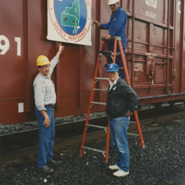 Photograph of exterior of Conrail Safety on Rails Theater boxcar 368191 with Philadelphia Division safety logo being installed, Oak Island Yard, Newark, NJ, summer 1992