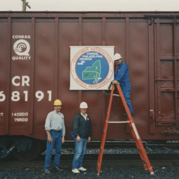 Photograph of exterior of Conrail Safety on Rails Theater boxcar 368191 with Philadelphia Division safety logo being installed, Oak Island Yard, Newark, NJ, summer 1992