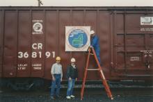 Photograph of exterior of Conrail Safety on Rails Theater boxcar 368191 with Philadelphia Division safety logo being installed, Oak Island Yard, Newark, NJ, summer 1992